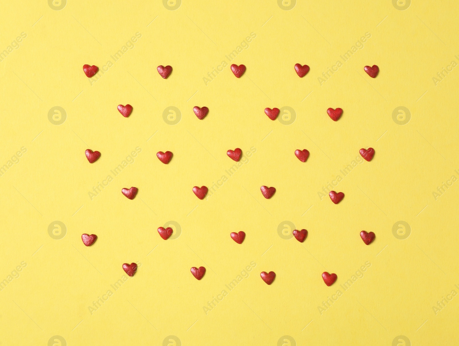 Bright heart shaped sprinkles on yellow background, flat lay Photo of Bright heart shaped sprinkles on yellow background, flat lay