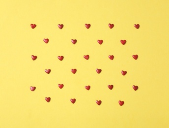 Bright heart shaped sprinkles on yellow background, flat lay Photo of Bright heart shaped sprinkles on yellow background, flat lay