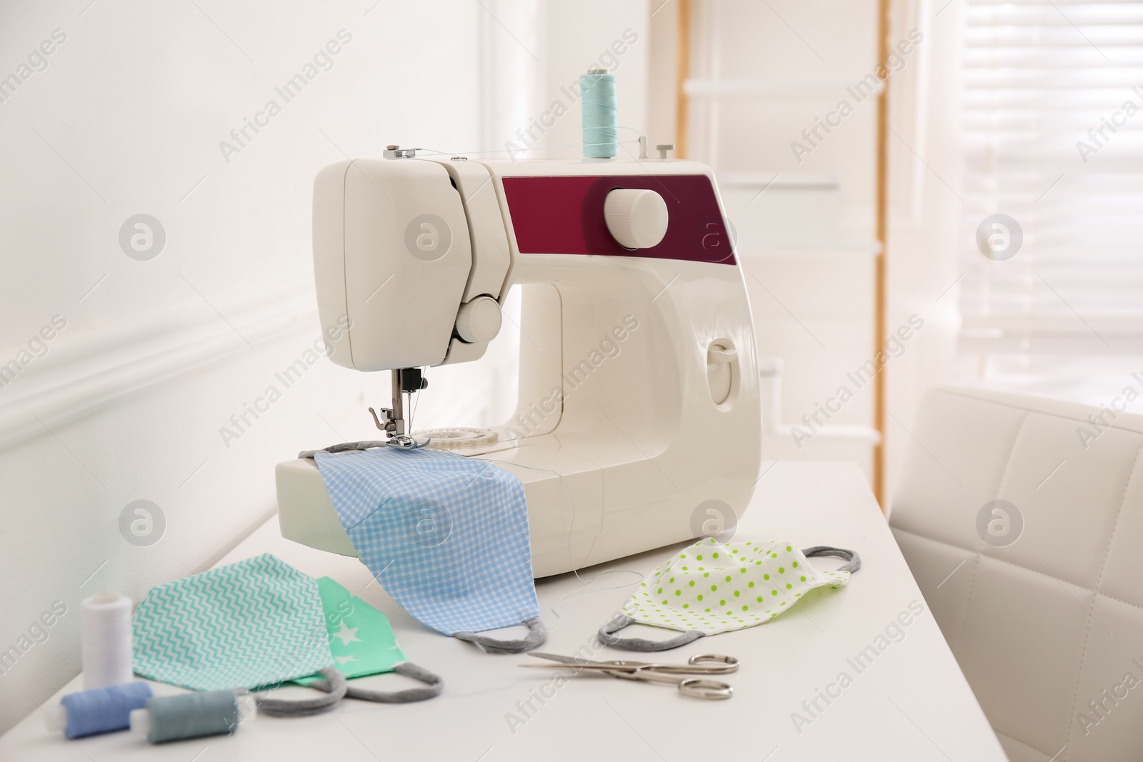Sewing machine with cloth mask on table indoors, space for text Photo of Sewing machine with cloth mask on table indoors, space for text