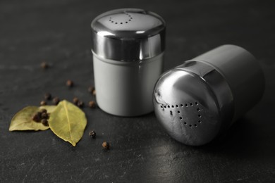Salt and pepper shakers with bay leaves on black table, closeup Photo of Salt and pepper shakers with bay leaves on black table, closeup