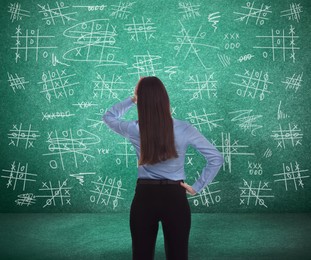 Young businesswoman near green chalkboard with drawn tic tac toe game, back view Image of Young businesswoman near green chalkboard with drawn tic tac toe game, back view
