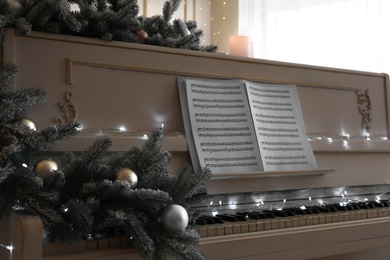 White piano with festive decor and note sheets indoors. Christmas music Photo of White piano with festive decor and note sheets indoors. Christmas music
