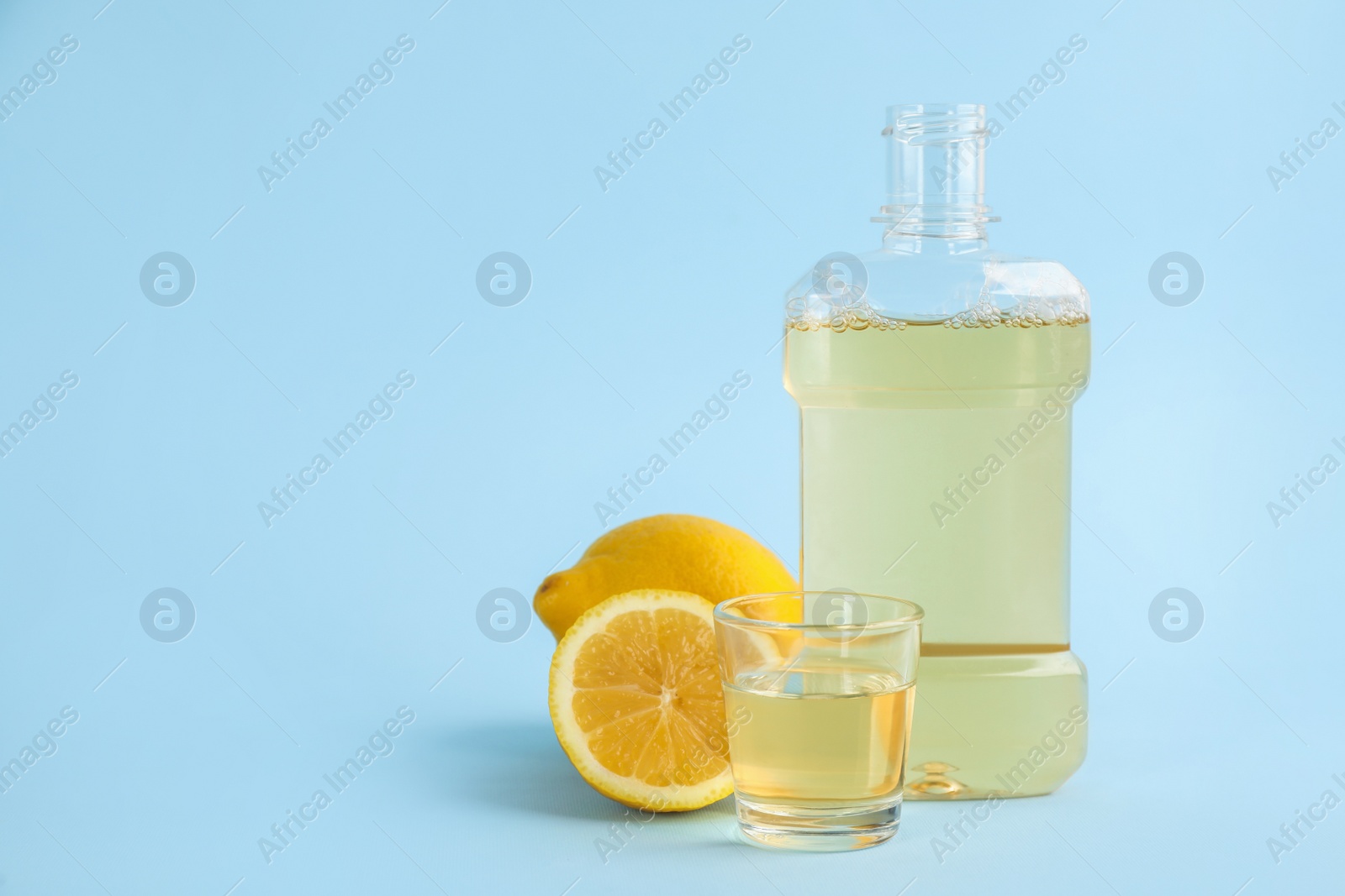 Mouthwash and fresh lemon on light blue background, space for text Photo of Mouthwash and fresh lemon on light blue background, space for text