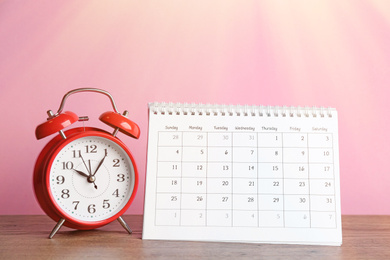Calendar and alarm clock on wooden table against pink background Image of Calendar and alarm clock on wooden table against pink background