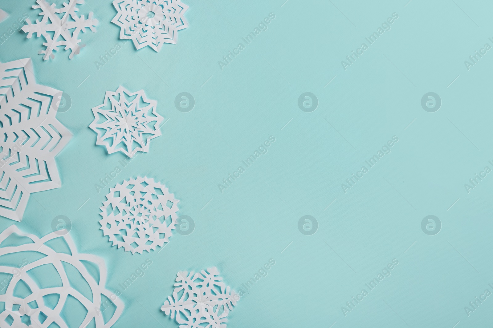 Flat lay composition with paper snowflakes on cyan background. Space for text Photo of Flat lay composition with paper snowflakes on cyan background. Space for text