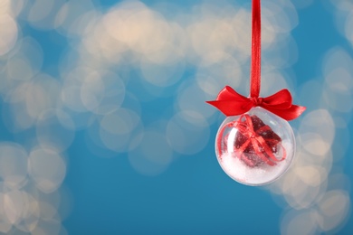 Decorative snow globe hanging against blurred festive lights, space for text Photo of Decorative snow globe hanging against blurred festive lights, space for text