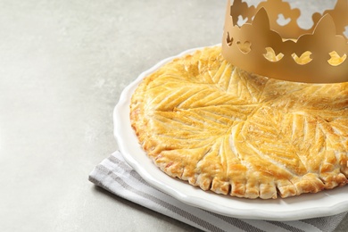 Traditional galette des Rois with paper crown on light grey table, closeup Photo of Traditional galette des Rois with paper crown on light grey table, closeup