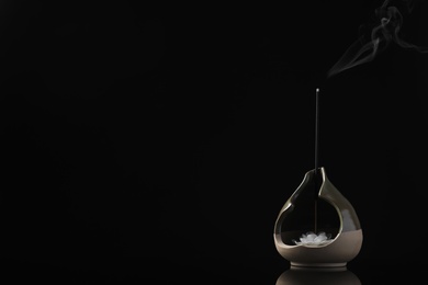 Incense stick smoldering in holder with lotus flower on black background. Space for text Photo of Incense stick smoldering in holder with lotus flower on black background. Space for text