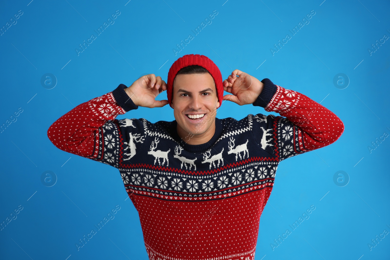 Handsome man in Christmas sweater and hat on blue background Photo of Handsome man in Christmas sweater and hat on blue background