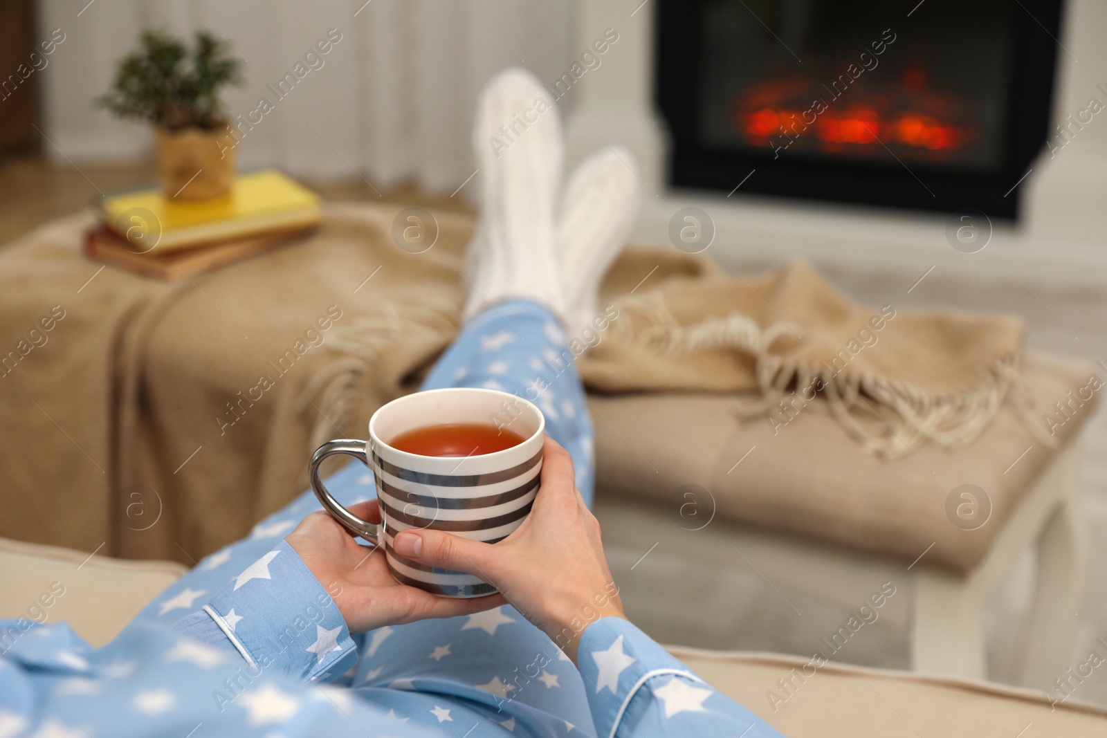 Woman with cup of tea resting near fireplace at home, closeup Photo of Woman with cup of tea resting near fireplace at home, closeup