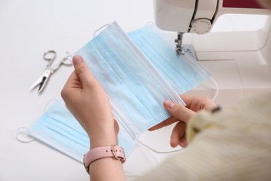 Woman making disposable mask with sewing machine at white table, closeup Photo of Woman making disposable mask with sewing machine at white table, closeup