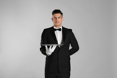 Handsome butler with tray on light grey background Photo of Handsome butler with tray on light grey background