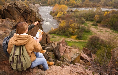 Couple of travelers with backpacks and map sitting on steep cliff. Autumn vacation Photo of Couple of travelers with backpacks and map sitting on steep cliff. Autumn vacation