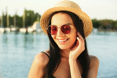 Beautiful young woman wearing stylish sunglasses near river Photo of Beautiful young woman wearing stylish sunglasses near river
