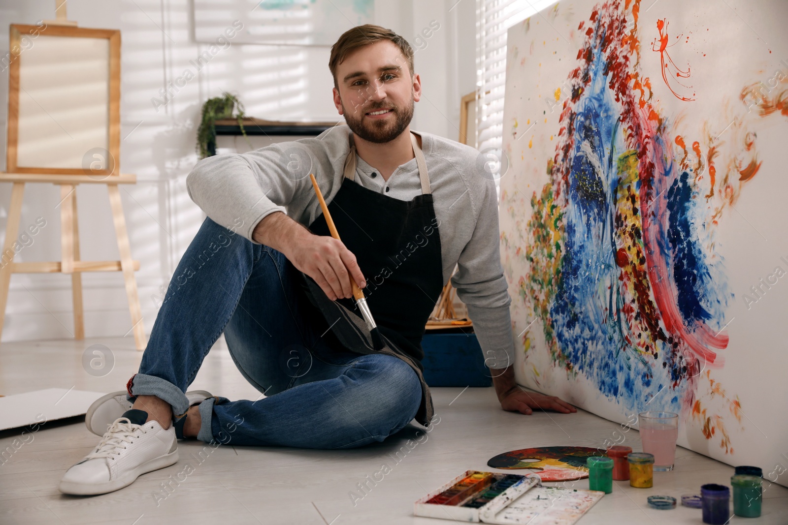 Young man with painting brush near canvas in artist studio Photo of Young man with painting brush near canvas in artist studio