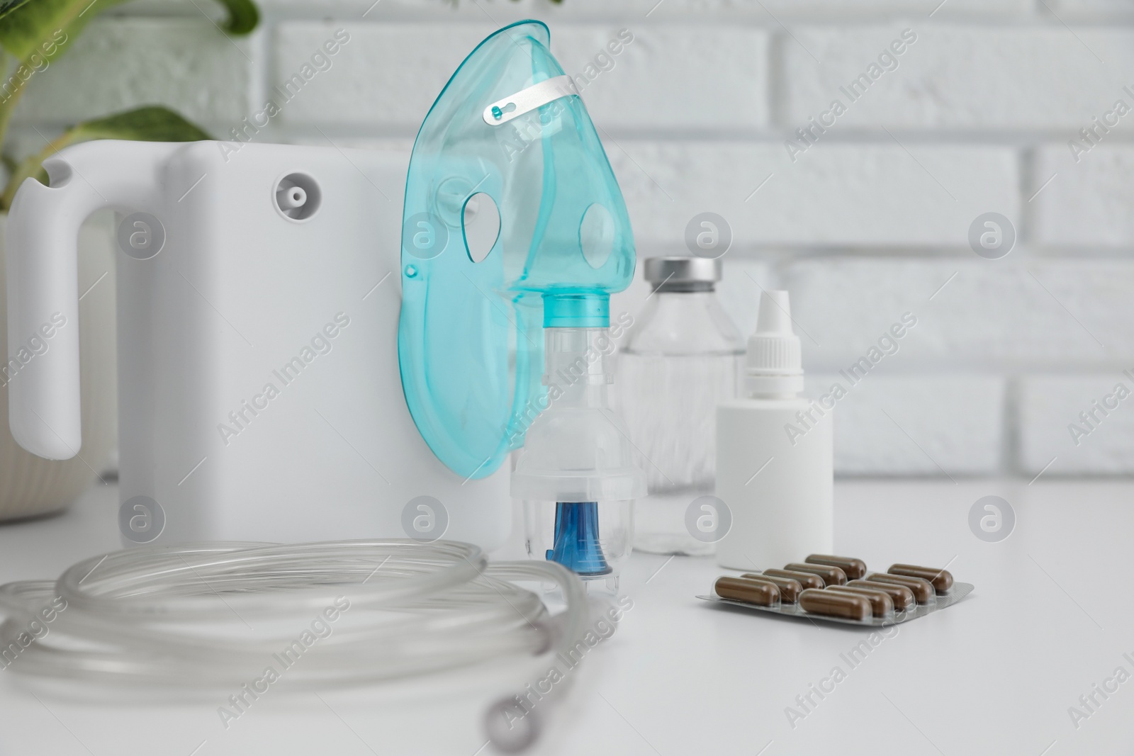 Photo of Modern nebulizer with face mask and medicines on white table near brick wall. Equipment for inhalation