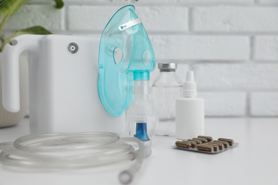 Modern nebulizer with face mask and medicines on white table near brick wall. Equipment for inhalation Photo of Modern nebulizer with face mask and medicines on white table near brick wall. Equipment for inhalation