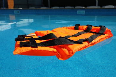 Bright orange life jacket floating in swimming pool Photo of Bright orange life jacket floating in swimming pool