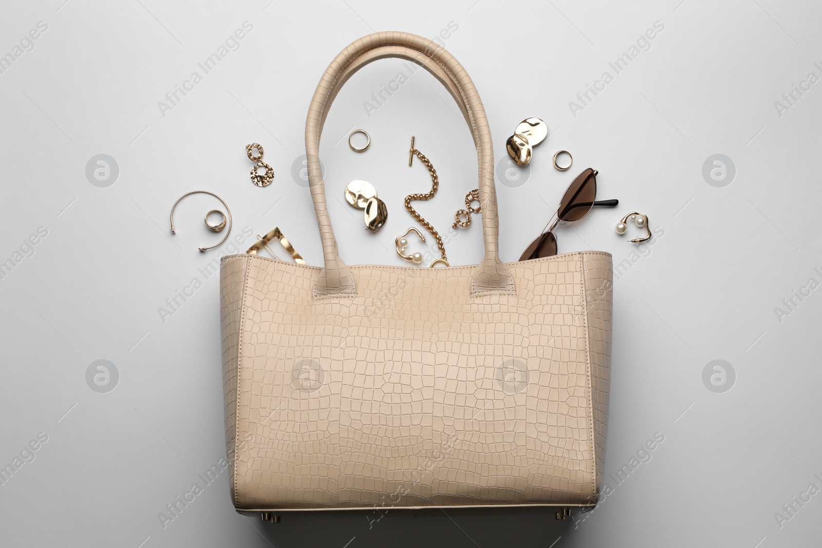 Stylish woman's bag, sunglasses and bijouterie on light background, flat lay Photo of Stylish woman's bag, sunglasses and bijouterie on light background, flat lay
