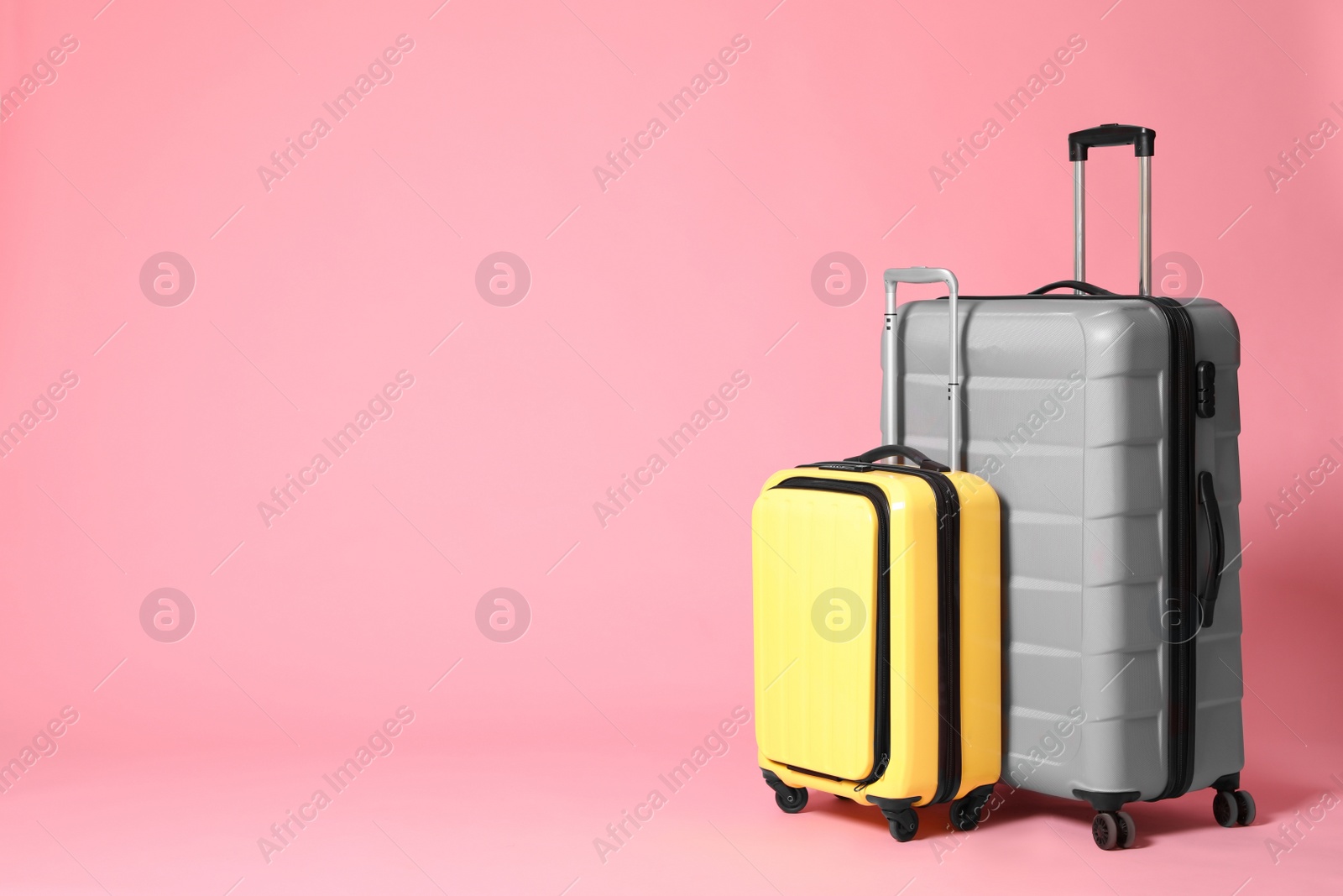 Photo of Stylish yellow and grey suitcases on pink background. Space for text
