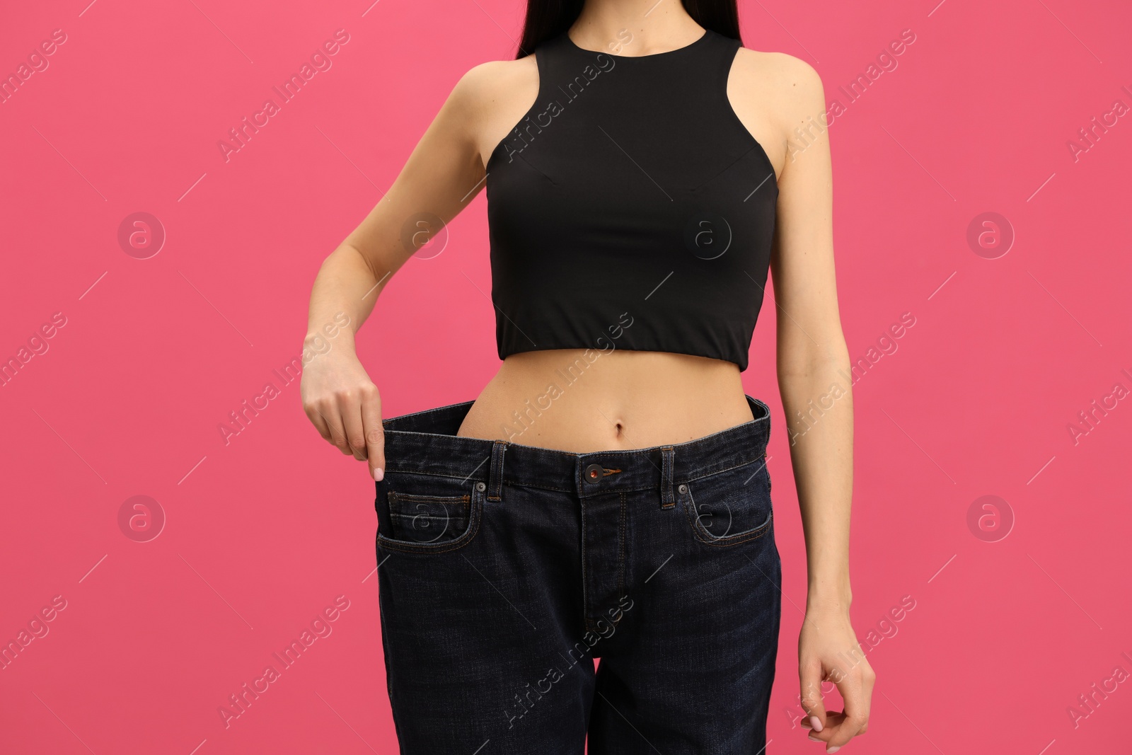 Young woman wearing big jeans after weight loss on pink background, closeup Photo of Young woman wearing big jeans after weight loss on pink background, closeup