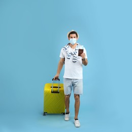 Male tourist in protective mask holding passport with ticket and suitcase on turquoise background Photo of Male tourist in protective mask holding passport with ticket and suitcase on turquoise background