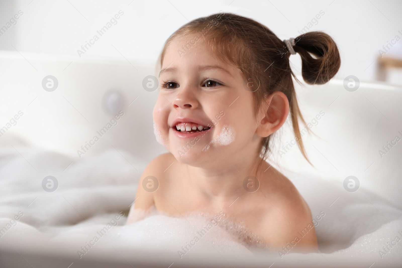 Photo of Cute little girl taking bubble bath at home