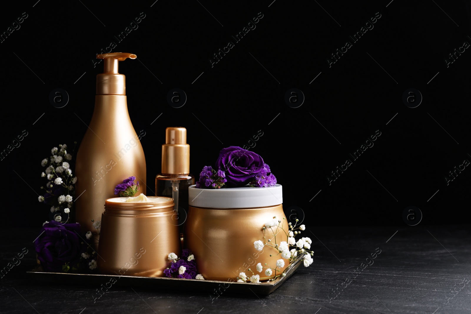 Set of hair cosmetic products and flowers on stone table against black background. Space for text Photo of Set of hair cosmetic products and flowers on stone table against black background. Space for text