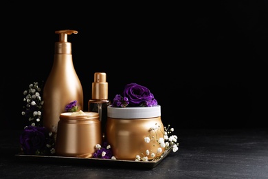 Set of hair cosmetic products and flowers on stone table against black background. Space for text Photo of Set of hair cosmetic products and flowers on stone table against black background. Space for text
