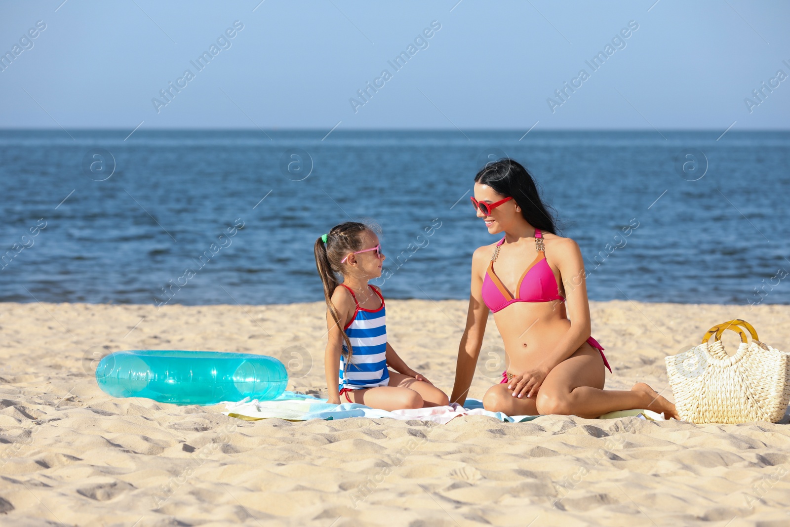 Happy mother and daughter on sandy beach near sea. Summer holidays with family Photo of Happy mother and daughter on sandy beach near sea. Summer holidays with family