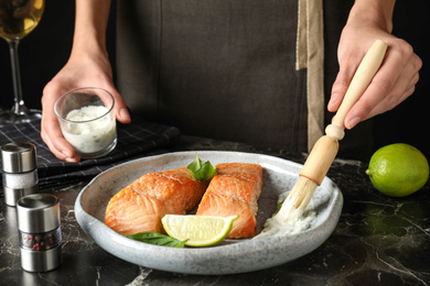 Woman adding sauce to cooked red fish on dark marble table, closeup Photo of Woman adding sauce to cooked red fish on dark marble table, closeup