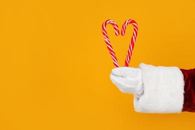 Santa Claus holding candy canes on yellow background, closeup of hand. Space for text Photo of Santa Claus holding candy canes on yellow background, closeup of hand. Space for text