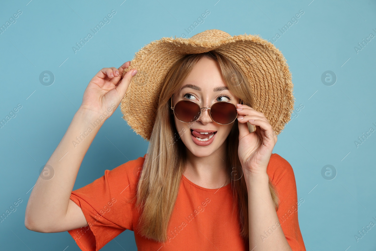 Beautiful young woman wearing straw hat and sunglasses on light blue background. Stylish headdress Photo of Beautiful young woman wearing straw hat and sunglasses on light blue background. Stylish headdress