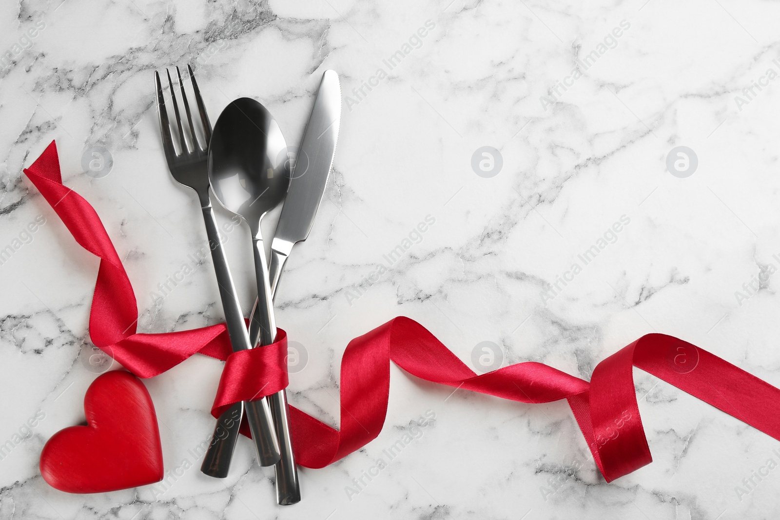 Cutlery set and red ribbon on white marble background, flat lay with space for text. Valentine's Day dinner Photo of Cutlery set and red ribbon on white marble background, flat lay with space for text. Valentine's Day dinner