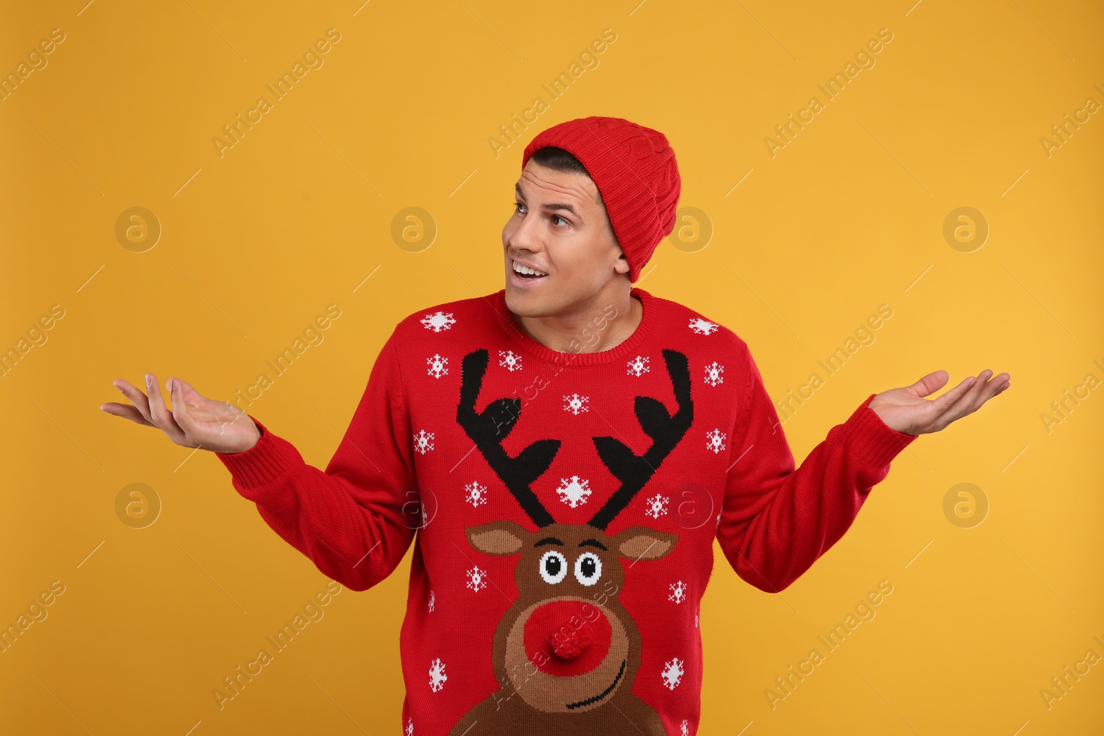 Emotional man in Christmas sweater and hat on yellow background Photo of Emotional man in Christmas sweater and hat on yellow background