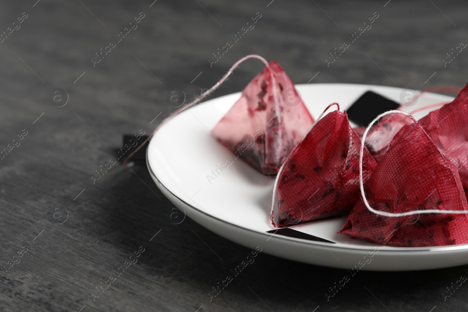 Saucer with used pyramid tea bags on grey table, closeup. Space for text Photo of Saucer with used pyramid tea bags on grey table, closeup. Space for text