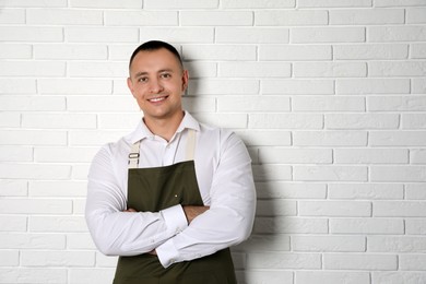 Portrait of happy young waiter in uniform near white brick wall, space for text Photo of Portrait of happy young waiter in uniform near white brick wall, space for text