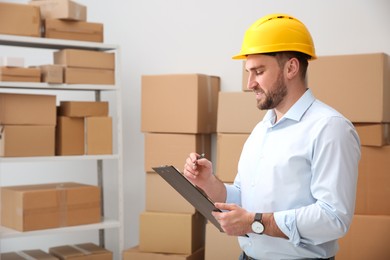 Young man with clipboard near cardboard boxes at warehouse Photo of Young man with clipboard near cardboard boxes at warehouse