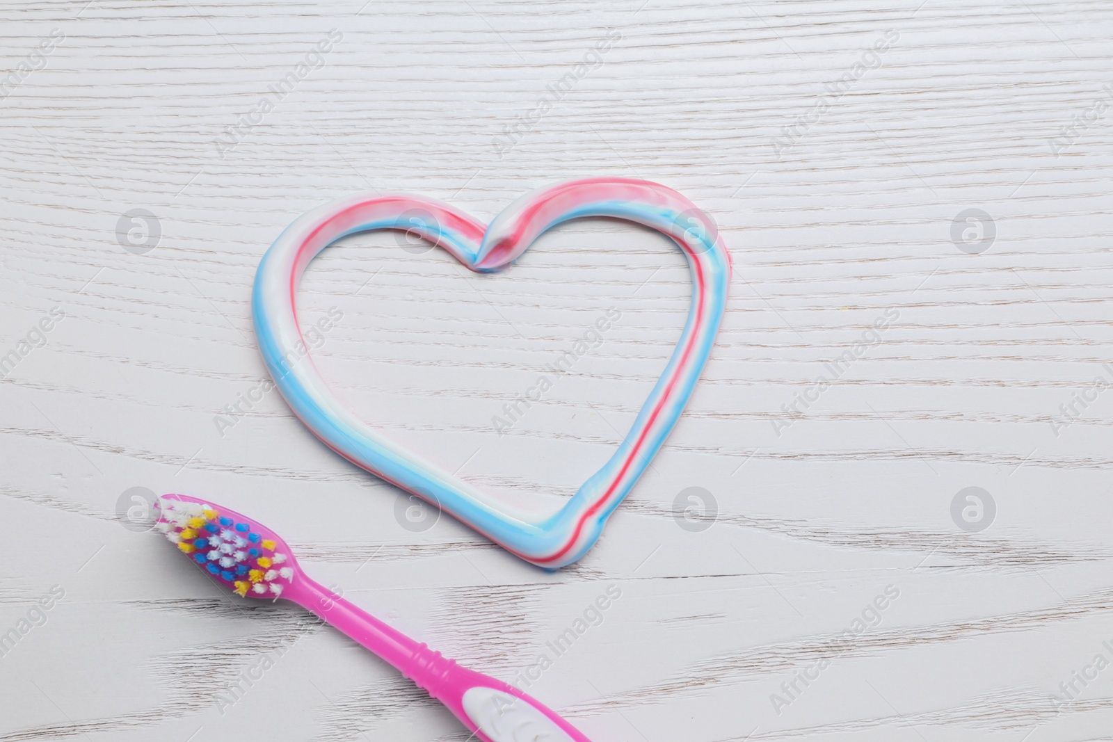 Photo of Heart made with toothpaste and brush on white wooden background, flat lay