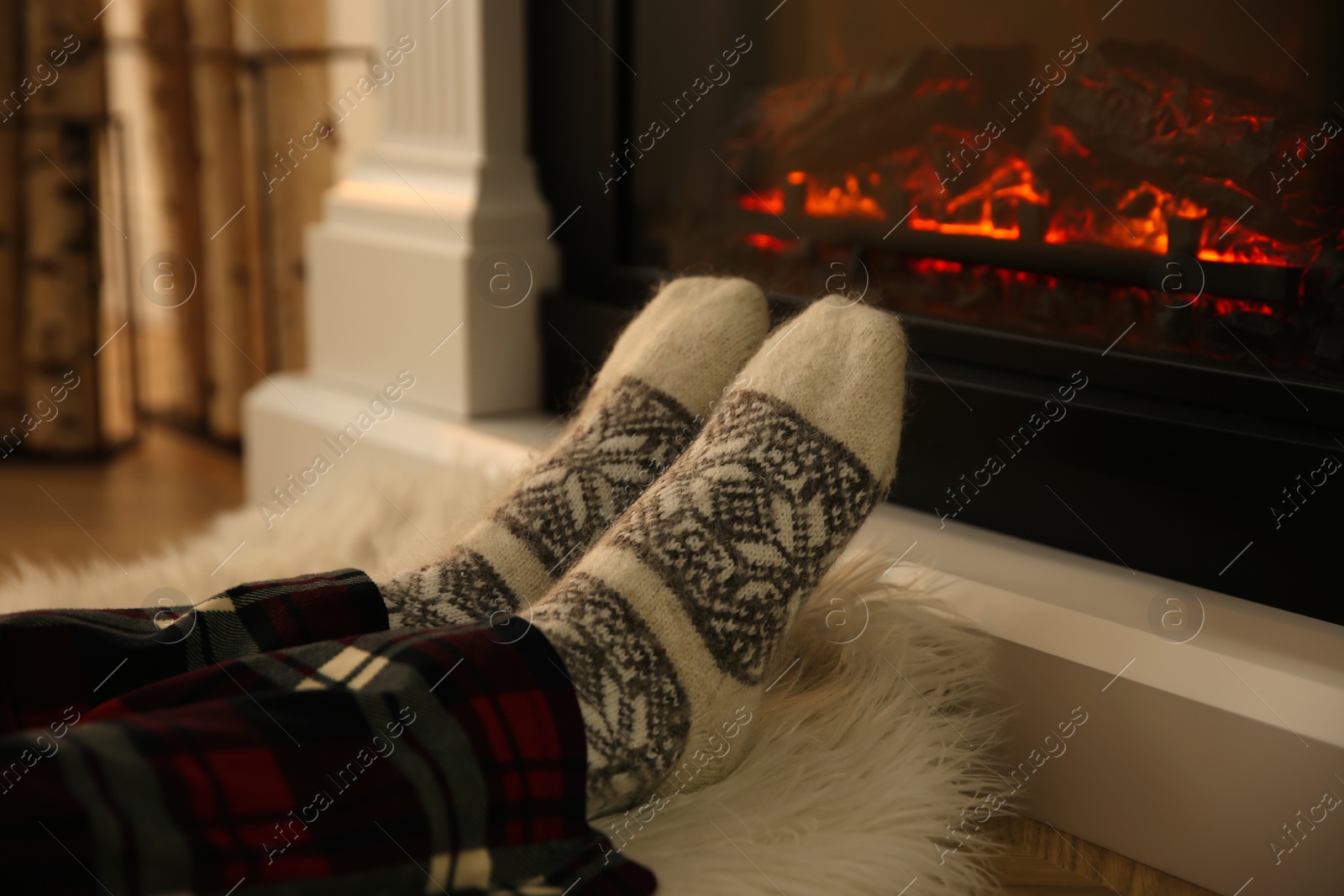 Photo of Woman in warm socks sitting near fireplace with burning wood at home, closeup