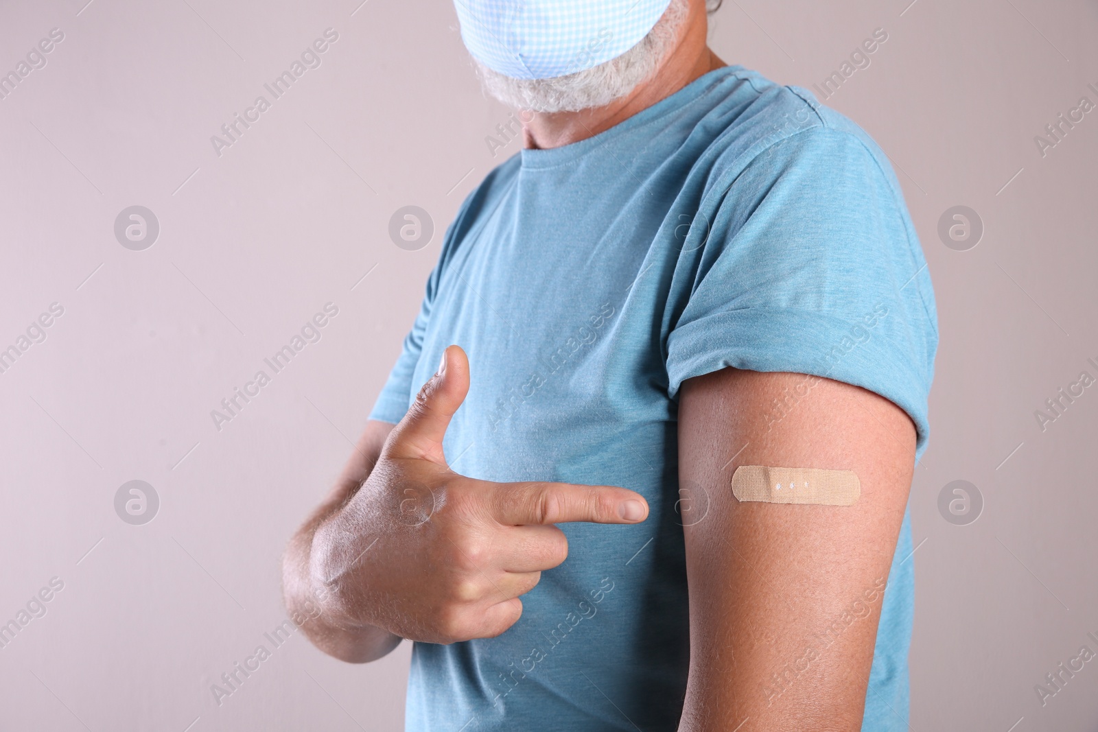 Senior man in protective mask pointing at arm with bandage after vaccination on beige background, closeup Photo of Senior man in protective mask pointing at arm with bandage after vaccination on beige background, closeup