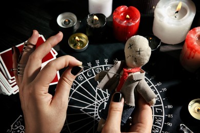 Woman stabbing voodoo doll with needle at table, closeup. Curse ceremony Photo of Woman stabbing voodoo doll with needle at table, closeup. Curse ceremony