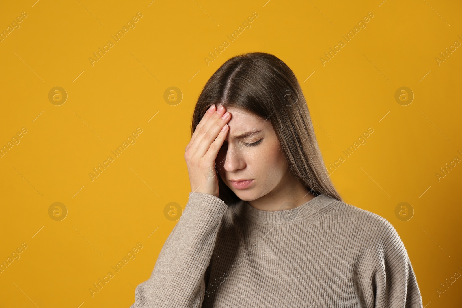 Young woman suffering from migraine on yellow background Photo of Young woman suffering from migraine on yellow background