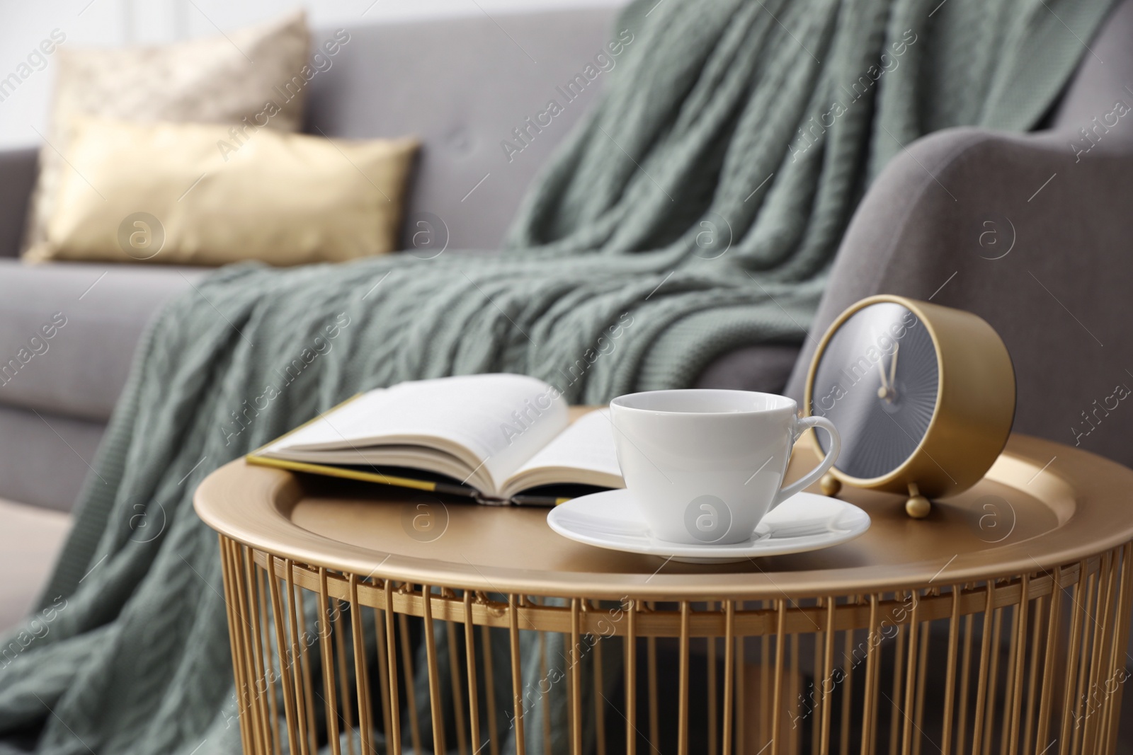 Coffee table with cup of tea, clock and book near sofa in room Photo of Coffee table with cup of tea, clock and book near sofa in room