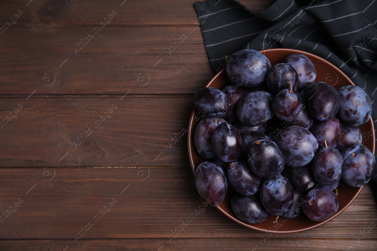 Delicious ripe plums in bowl on wooden table, top view. Space for text Photo of Delicious ripe plums in bowl on wooden table, top view. Space for text
