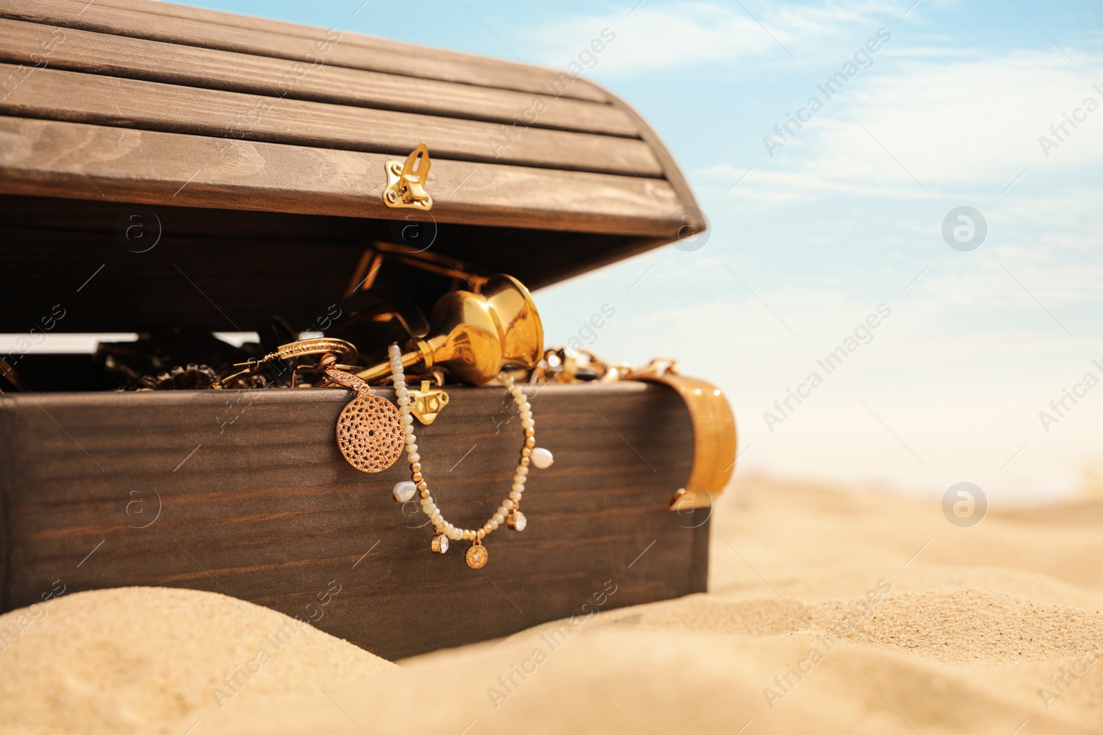 Open wooden chest with treasures on sandy beach, space for text Photo of Open wooden chest with treasures on sandy beach, space for text