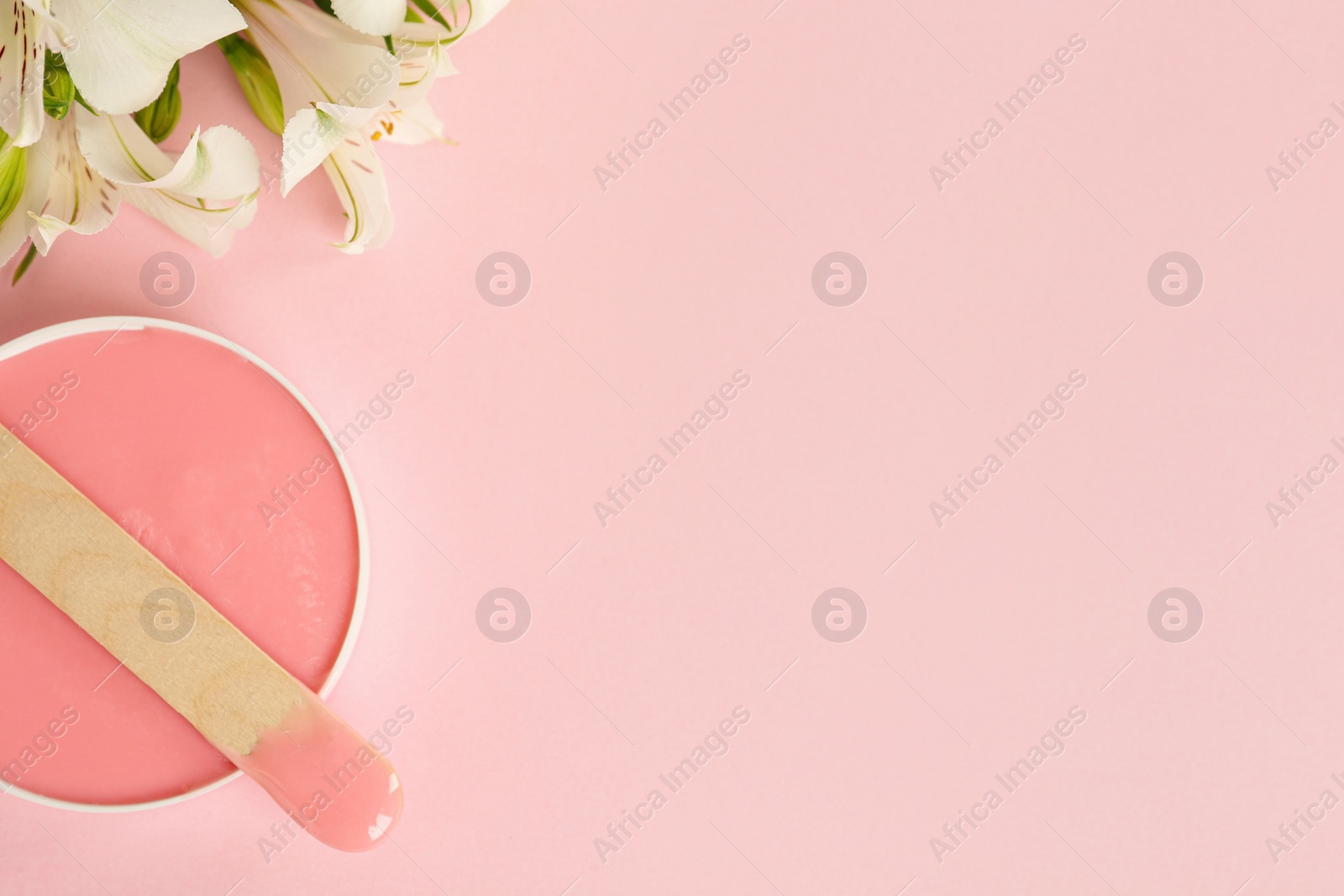 Photo of Wooden spatula, hot depilatory wax and flowers on light pink background, flat lay. Space for text