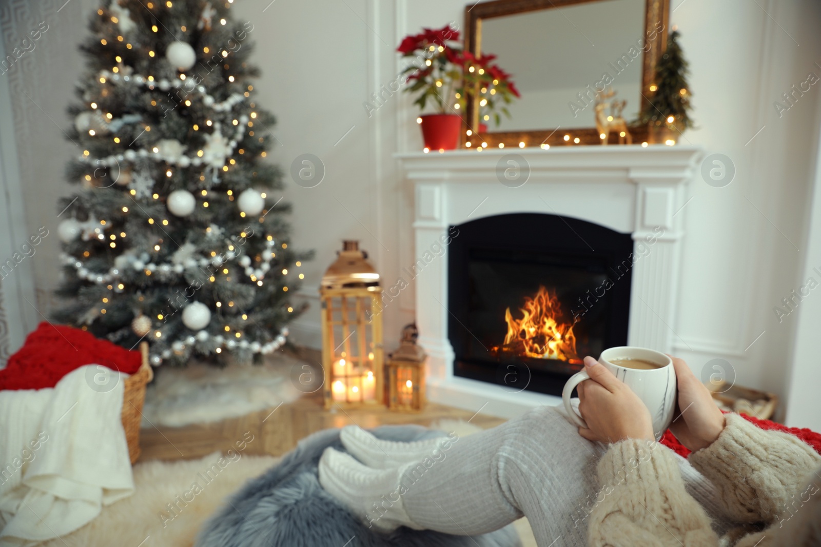Woman with hot drink resting near fireplace in cozy room decorated for Christmas, closeup Photo of Woman with hot drink resting near fireplace in cozy room decorated for Christmas, closeup