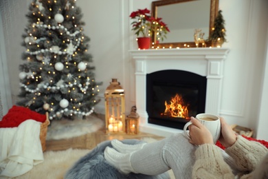 Woman with hot drink resting near fireplace in cozy room decorated for Christmas, closeup Photo of Woman with hot drink resting near fireplace in cozy room decorated for Christmas, closeup