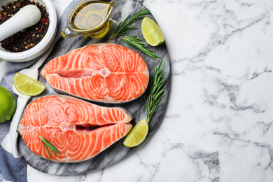 Photo of Top view of fresh raw salmon and products on white marble table, space for text. Fish delicacy